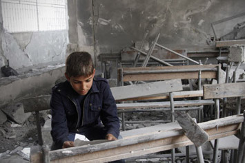 Syrian boy reads a torn paper inside his destroyed school classroom © AP / Reporters 